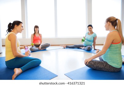 pregnancy, sport, fitness, people and healthy lifestyle concept - group of happy pregnant women with water bottles sitting on mats and talking in gym
