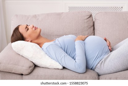 Pregnancy And Stomach Spasms. Pregnant Lady Suffering From Abdominal Pain Touching Belly Lying On Sofa Indoor