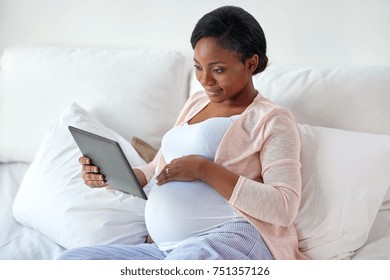 pregnancy, technology, people and expectation concept - happy pregnant african american woman with tablet pc computer in bed at home
