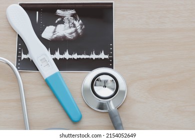 Pregnancy test showing a positive result and stethoscope, ultrasound picture of baby isolated on wooden background. Result of ultrasound picture, ultrasonography for pregnancy. Pregnancy care concept.
