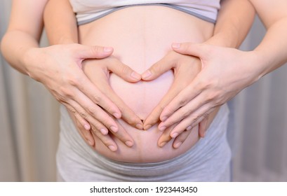 Pregnancy woman with husband at home. Love couple using their hands to mark the heart shape.