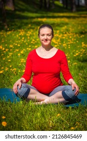 Pregnancy yoga exercise - pregnant woman doing asana Sukhasana easy yoga pose outdoors on grass lawn with dandelions in summer