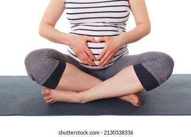 Pregnancy yoga exercise - pregnant woman doing asana Sukhasana easy yoga pose showing heart symbol with her hands isolated on white background