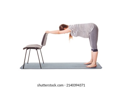 Pregnancy yoga exercise - pregnant woman doing yoga asana Uttanasana Standing Forward Fold Pose with hands on chair easy variation isolated on white background