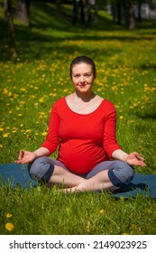 Pregnancy yoga exercise - pregnant woman doing asana Sukhasana easy yoga pose with chin mudra outdoors on grass lawn with dandelions in summer