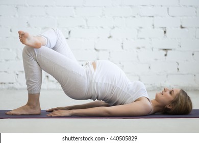 Pregnancy Yoga and Fitness concept. Beautiful young pregnant yoga model working out indoor. Pregnant happy fitness person practicing yoga at home. Prenatal one legged variation of shoulder bridge pose