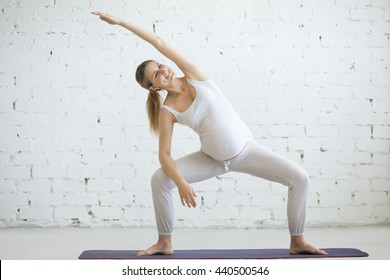 Pregnancy Yoga, Fitness concept. Portrait of beautiful young pregnant yoga model working out indoor. Pregnant happy fitness person enjoy yoga practice at home. Prenatal side bending in Sumo Squat Pose