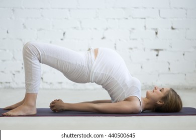 Pregnancy Yoga and Fitness concept. Portrait of young pregnant yoga model working out indoors. Pregnant happy fitness person enjoy yoga practice at home. Prenatal shoulder bridge exercise. Full length - Powered by Shutterstock