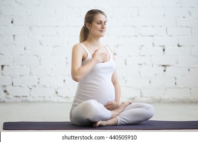 Pregnancy Yoga and Fitness concept. Portrait of young pregnant yoga model working out indoors. Pregnant fitness person smiling while practicing yoga at home. Prenatal breathing with closed eyes
