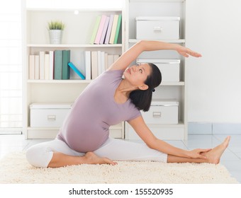 Pregnancy yoga meditation. Full length healthy 8 months pregnant calm Asian woman meditating or doing yoga exercise at home. Relaxation yoga sitting side stretch positions.