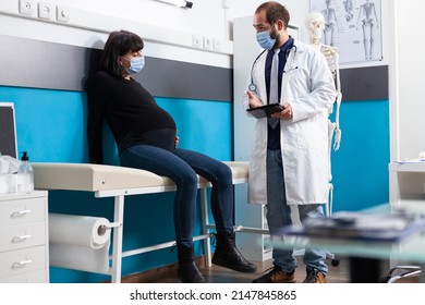 Pregnant Adult Talking About Childbirth With Health Physician During Covid 19 Pandemic. General Practitioner Doing Consultation With Woman Expecting Child At Checkup Visit In Medical Cabinet.