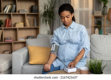 Pregnant African American Lady Measuring Arterial Blood Pressure Having Hypertension Problem Expecting Baby Sitting On Couch At Home. High And Low Tension Symptom Concept