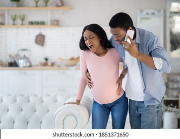 Pregnant African American woman having prenatal contractions, worried husband calling doctor on smartphone. Black lady giving birth to baby, her partner arranging medical help