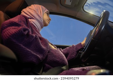 Pregnant arabic muslim woman driving car at night wearing winter clothes ,hijab and seat belt driving in confidently and feeling safe - Powered by Shutterstock