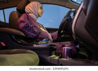 Pregnant arabic muslim woman driving car at night wearing winter clothes ,hijab and seat belt driving in confidently and feeling safe - Powered by Shutterstock