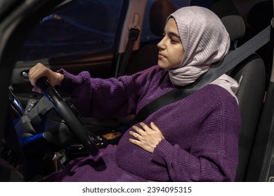 Pregnant arabic muslim woman driving car at night wearing winter clothes ,hijab and seat belt driving in confidently and feeling safe - Powered by Shutterstock