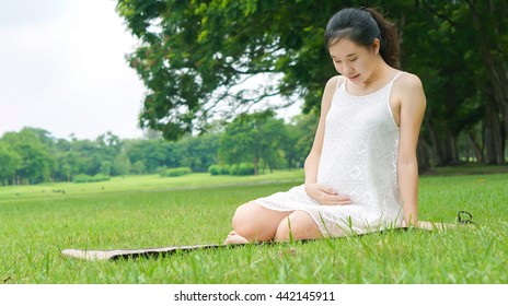 Pregnant Asia woman sitting, smiling and relaxing on green field in the park