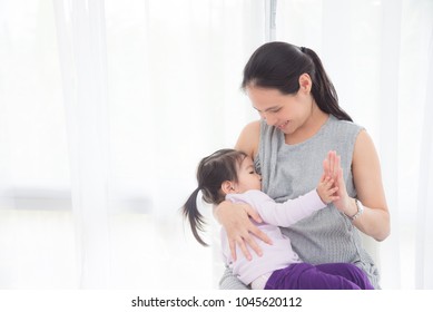 Pregnant asian mother breast feeding her daughter at home