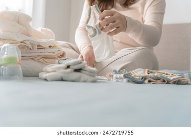 Pregnant asian woman getting ready for the maternity hospital preparing and planning baby clothes for new baby of pregnancy packing baby stuff on bed. - Powered by Shutterstock