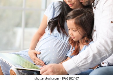 Pregnant Asian Woman With Her Family Reading Book At Home