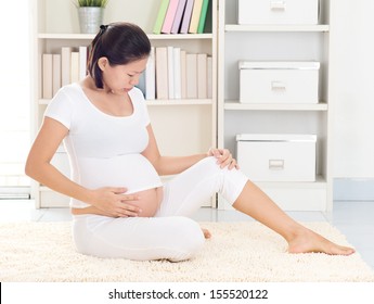 Pregnant Asian Woman At Home With Cramp Leg. Woman Health Concept.