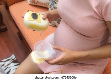 Pregnant asian woman learning how to use electric breast pump for the first time
