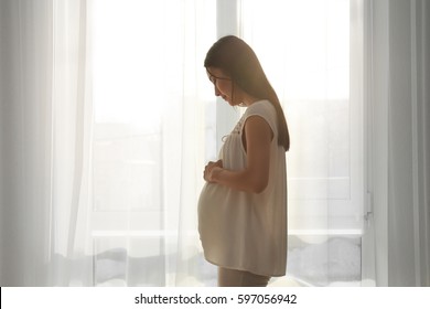 Pregnant Asian Woman Standing Near Window At Home