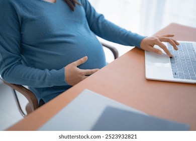 Pregnant asian woman using laptop at home pregnant businesswoman typing on laptop working on remote project in home office pregnancy concept. - Powered by Shutterstock