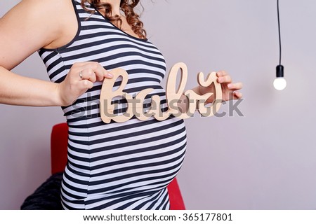Pregnant belly with symbol text baby in her hands.