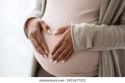 Pregnant black woman holding palms in heart shape on her big tummy, cropped. Unrecognizable african american expecting lady standing by window at home. Pregnancy and maternity concept - Powered by Shutterstock