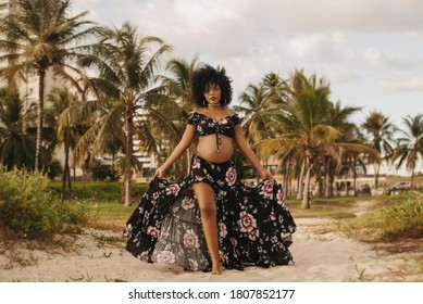 pregnant black woman on the beach with beautiful flowery dress