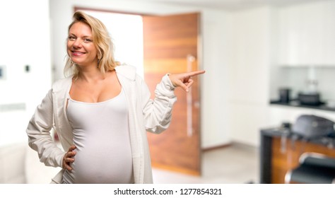 Pregnant blonde woman with white sweatshirt pointing finger to the side and presenting a product in her house - Shutterstock ID 1277854321
