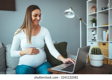 Pregnant businesswoman with hand on stomach working at desk. Female professional is wearing business casuals. She is using laptop in office. Cropped shot of an attractive young pregnant woman working - Powered by Shutterstock