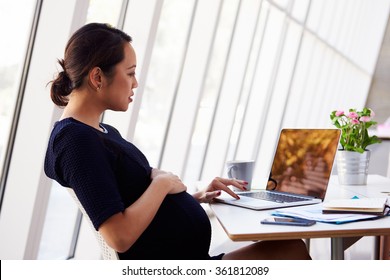 Pregnant Businesswoman Using Laptop In Office