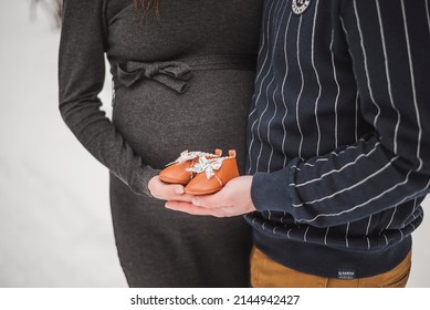 Pregnant couple holding baby shoes near belly of expecting mother outdoor in the winter snow