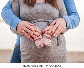  pregnant couple placing baby shoes on woman big 9 month belly outdoor. Planned pregnancy and a new social unit - Powered by Shutterstock