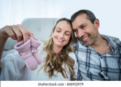 Pregnant couple sitting on floor holding baby shoes in living room