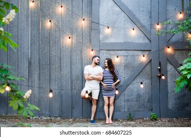A pregnant couple is standing by the barn, flirting