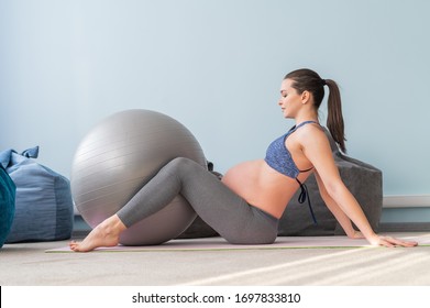 Pregnant european woman performs exercises with fitness ball. Expectant mother is doing yoga in the 3rd trimester. Girl in the classroom in preparation for childbirth. - Powered by Shutterstock