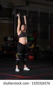 Pregnant Female Athlete Doing Dumbbell Power Snatch Overhead Press Workout In Dark Gym