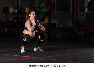 Pregnant female athlete doing goblet squats with kettlebell in dark gym - Powered by Shutterstock