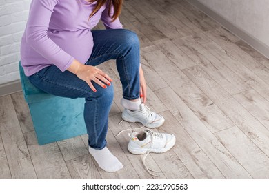 A pregnant girl with a big belly puts on sneakers on her feet. The concept of discomfort and inconvenience when bending over and putting on shoes. Convenient and comfortable shoes for pregnant women. - Shutterstock ID 2231990563