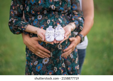 pregnant girl and her husband are holding baby shoes near the belly
