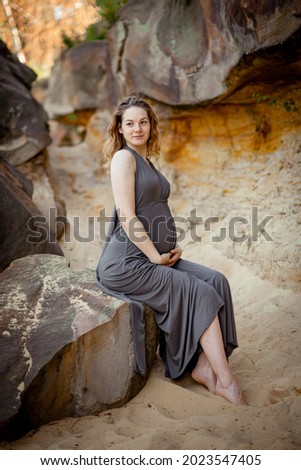 pregnant girl in a long gray dress sits on a stone among rocks and sand