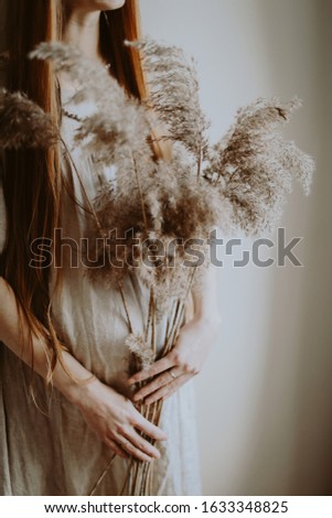 pregnant girl with long hair in a gray linen dress holds ears in her hands


