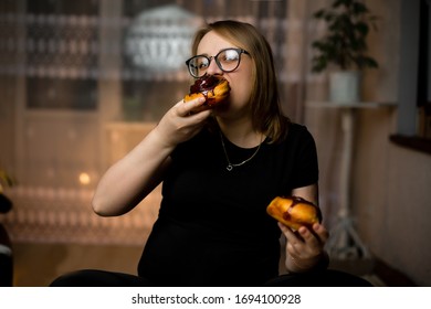 A Pregnant Girl Is Sitting And Eating Fresh Cinnamon Rolls. Close-up, General Plan. Dark Clothes. Space For Text