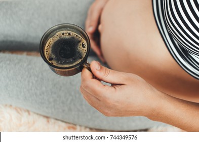 pregnant girl sitting on bed with coffee Cup in hand coffee
