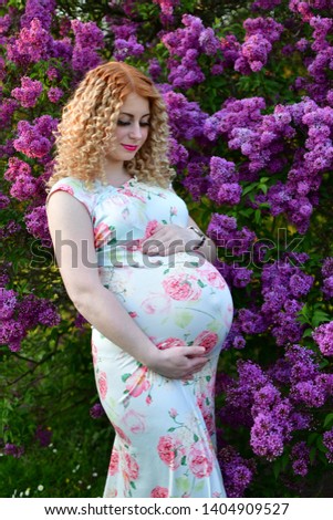 pregnant girl smiling in a blooming spring park, the girl is walking in a  syringa vulgaris flowers park