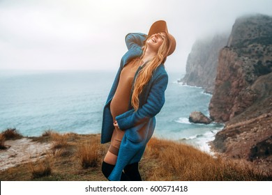 Pregnant girl wearing coat and hat traveling in mountains. Cold weather, calm scene. Happy and healthy maternity. Wanderlust photo series.