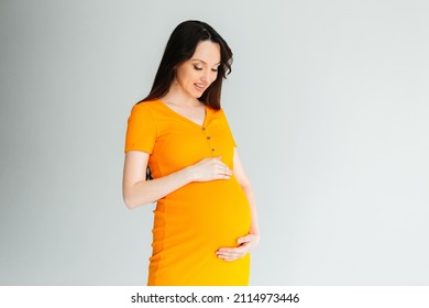 Pregnant happy woman in a bright orange dress on a gray background
